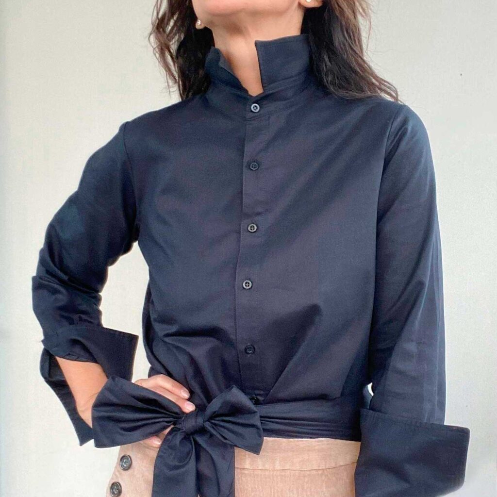 Clásica NEGRA es una camisa con cuello terminado en punta y mangas largas. Inspiración romántica, clásica y minimalista al mismo tiempo. Un modelo Versátil que puedes usar de diferentes formas según el estilo que quieras llevar, elegante, casual, deportiva. El detalle no va solo en su cuello y puños largos almidonados que te permiten jugar al recogerla o al lucirla en toda su extensión, sino que también, lleva un su listón que puedes combinar a tu estilo y darle tu personalidad.