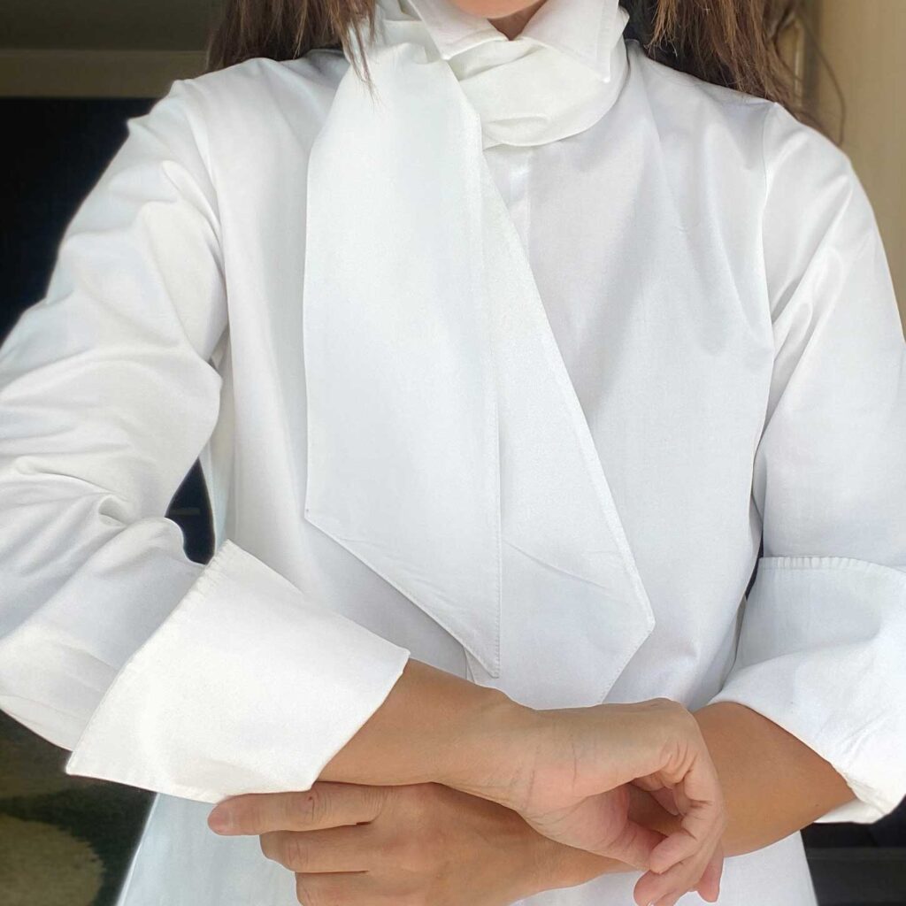 Clásica BLANCA es una camisa con cuello terminado en punta y mangas largas. Inspiración romántica, clásica y minimalista al mismo tiempo. Un modelo Versátil que puedes usar de diferentes formas según el estilo que quieras llevar, elegante, casual, deportiva. El detalle no va solo en su cuello y puños largos almidonados que te permiten jugar al recogerla o al lucirla en toda su extensión, sino que también, lleva un su listón que puedes combinar a tu estilo y darle tu personalidad.